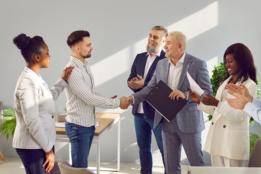 client and CEO shaking each others hands in agreement while co-workers watch in amazement.